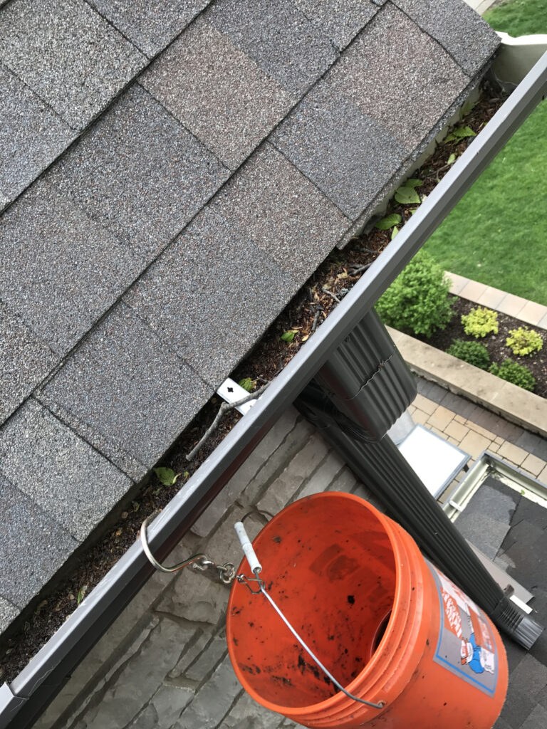 Orange bucket is hanged on the gutters for gutter cleaning