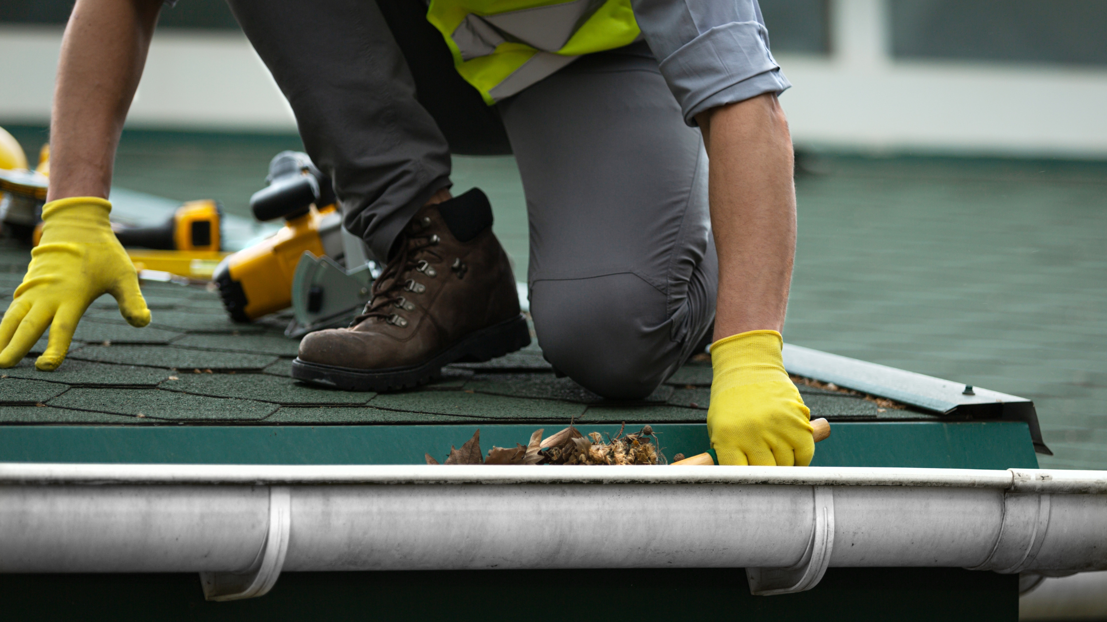 Worker cleaning out gutters by hand on a residential roof in the Gold Coast, wearing gloves and safety boots