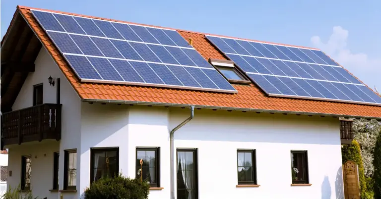 Large rooftop solar panel array installed on a terracotta tiled roof above clean gutters and downpipes on a two-story white home under a clear sky